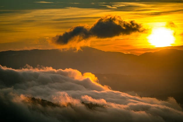 Bright sun setting behind mountains with dramatic sky on background