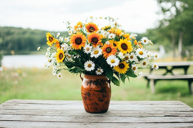 Bright sunflowers and daisies in a large vase on a picnic table