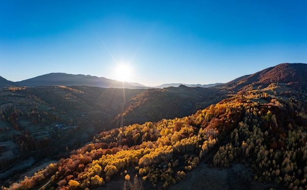 Bright sunrise at high mountains covered with autumn forest