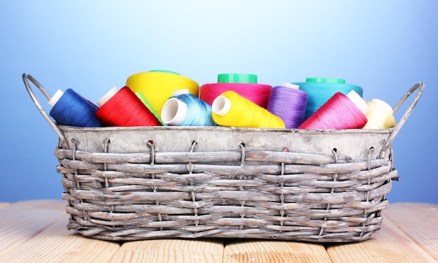 Bright threads in basket on wooden table on blue background