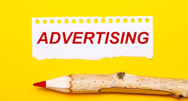 Photo on a bright yellow background a large wooden pencil and a sheet of torn paper with the text advertising