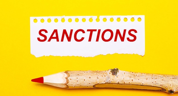 On a bright yellow background a large wooden pencil and a sheet of torn paper with the text SANCTIONS