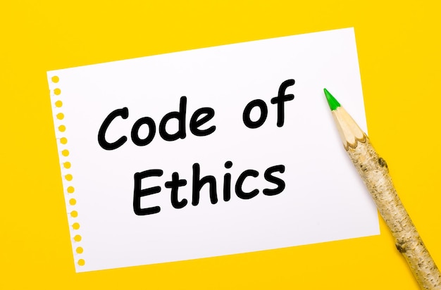 On a bright yellow background, a large wooden pencil and a white sheet of paper with the text CODE OF ETHICS