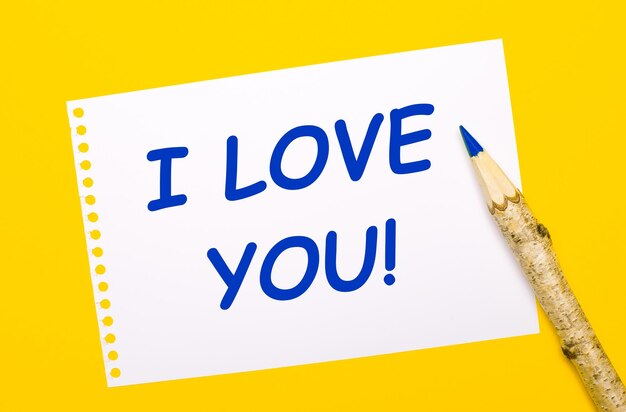 On a bright yellow background a large wooden pencil and a white sheet of paper with the text I LOVE YOU