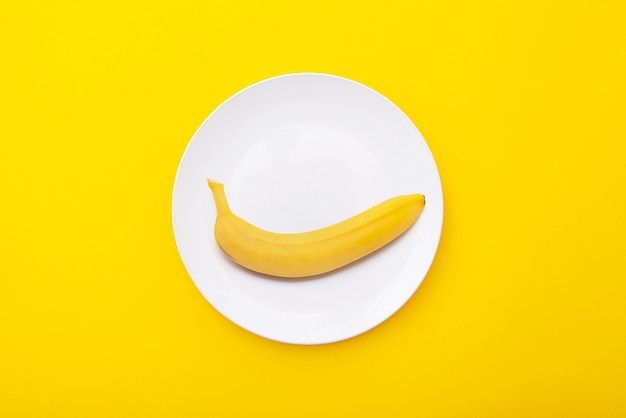 Bright yellow banana on white ceramic plate Creative minimal composition