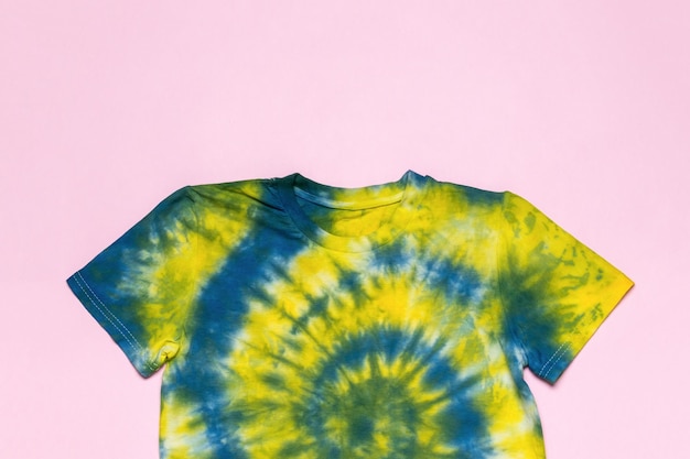 A bright yellow and blue tie dye Tshirt on a pink background Flat lay