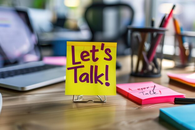 Bright Yellow Sticky Note with Lets Talk Message on Office Desk with Laptop