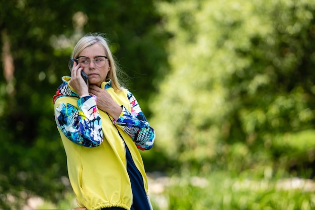 Brightly dressed blonde mature woman talking on smartphone in garden online communication concept