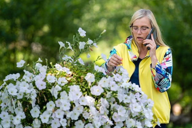 Brightly dressed blonde mature woman talking on smartphone in garden online communication concept