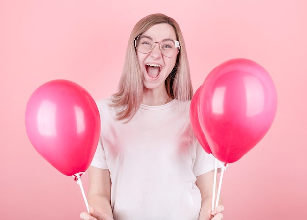 Broad smile. A close-up photo of a young charming lady in a white T-shirt who laughs with joy surrounded by pink balloons.