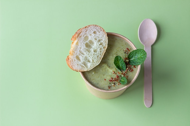 Broccoli cream soup with bread, mint and spices in craft container. Soup to go, healthy food delivery.