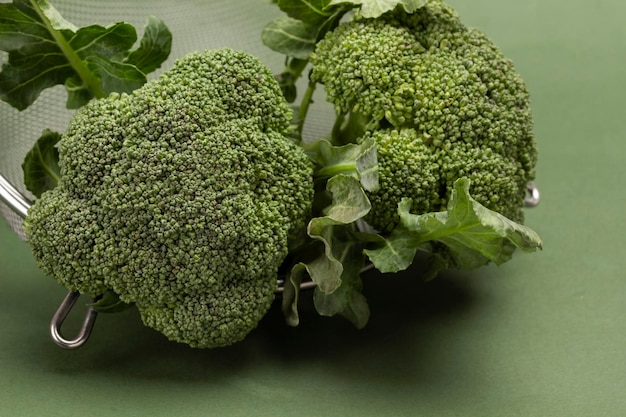 Broccoli in metal colander Close up Top view Green background