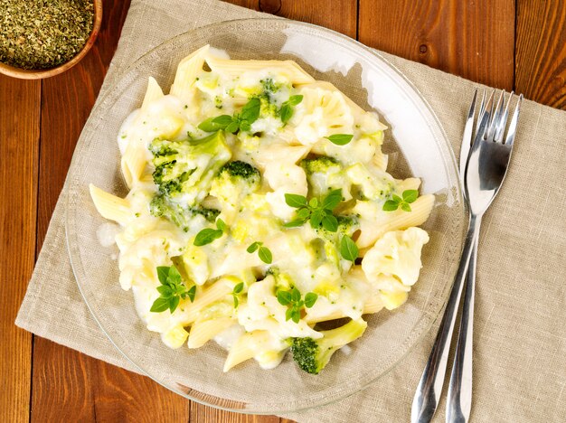 Broccoli pasta in glass plate on dark brown wooden table, top view.