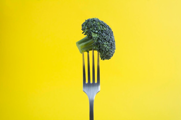 Broccoli stabbed on a silver fork on the yellow background Closeup Copy space