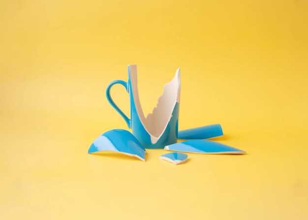 A broken blue cup with shards around on a yellow background