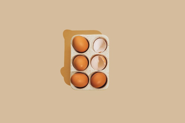 Broken brown raw chicken egg with egg shell in a ceramic storage tray on a beige background with copy space Creative Easter or food holiday decor and spring greeting card Flat lay