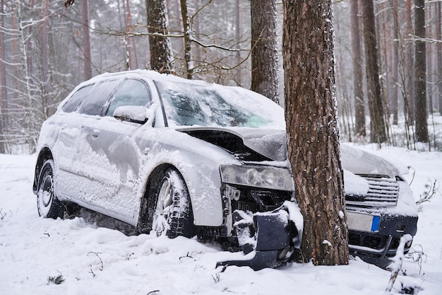 Broken car crashes into tree after losing control on slippery road in snowy forest. Abandoned car after accident