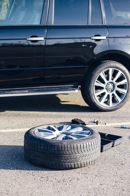 Broken car tire lies on the road next to repair tools and a black car in Russia close up