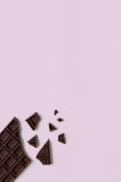 Broken chocolate bar on the pink background with copy space