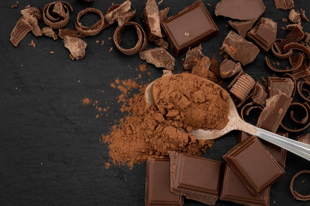 Broken chocolate pieces and cocoa powder on a dark background. Top view with copyspace.