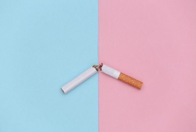 Broken cigarette on pink blue background. Quitting smoking