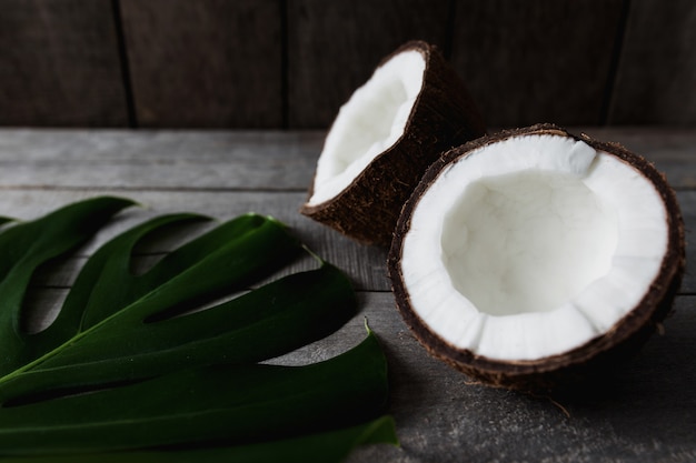 Broken coconuts, gray wooden background, monstera palm leaf. White coconut pulp. High quality photo