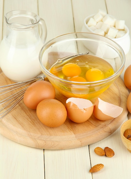 Broken egg in bowl and various ingredients next to them on wooden table closeup