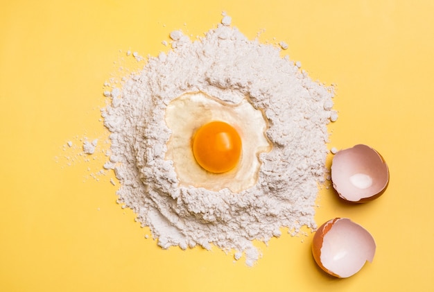 Photo broken egg yolk on flour for the dough on yellow background. baking concept.