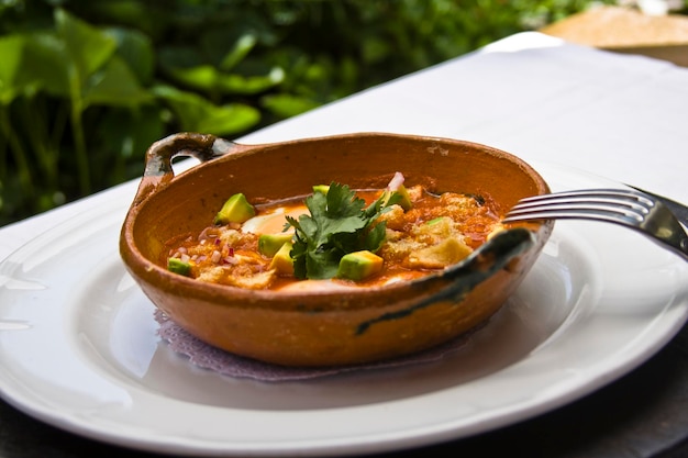 broken eggs, dish of broken eggs in tomato broth accompanied by pork rinds, and avocado on a table