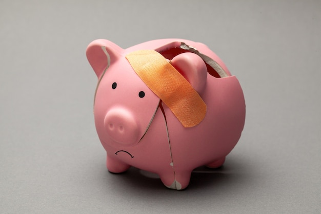 Broken piggy bank with band-aid on gray background.