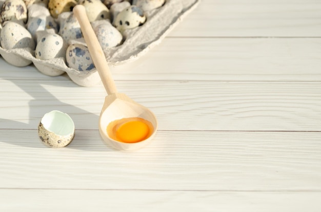 Broken quail egg with bright orange yolk in wooden spoon among whole quail eggs Space for text