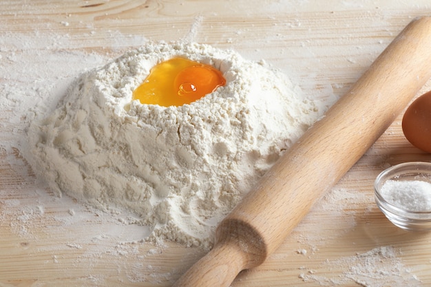 Broken raw egg in flour and rolling pin