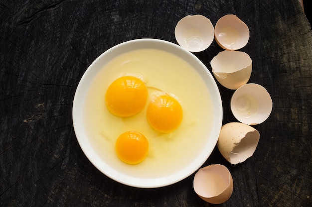 Broken raw eggs on white plate cracked shell on dark wooden desk