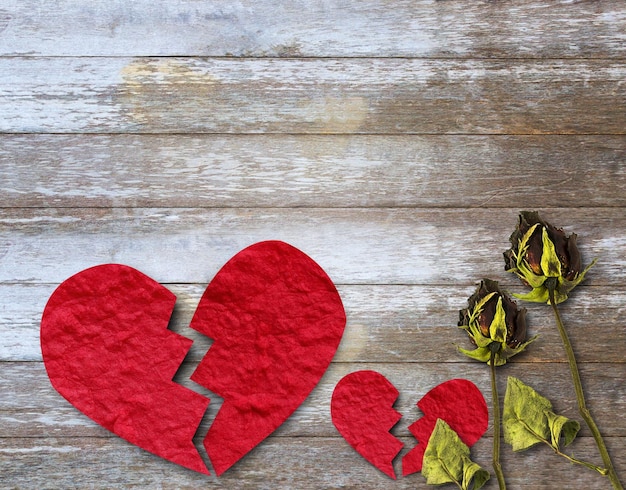 Broken red paper heart and dry rose on wood table