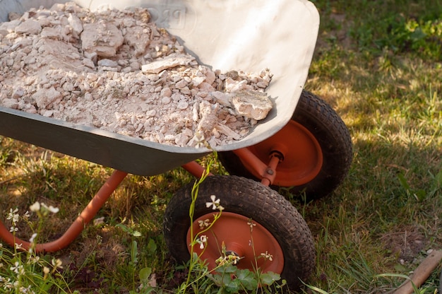 Broken rubble in a metal construction wheelbarrow on wheels on the grass