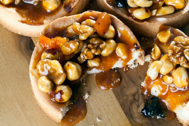 Broken with crumbs tartlet round shape with nuts and dried fruits poured with caramel, for the preparation of tartlets used ingredients hazelnuts, peanuts, dried apricot, dried plum, walnut