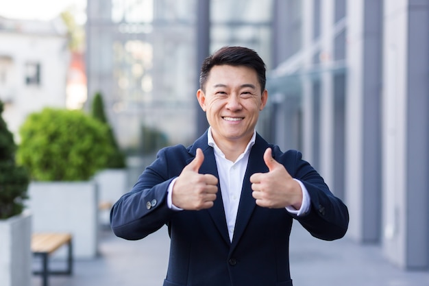 Broker asian businessman in business suit happy looking at camera and showing thumbs up