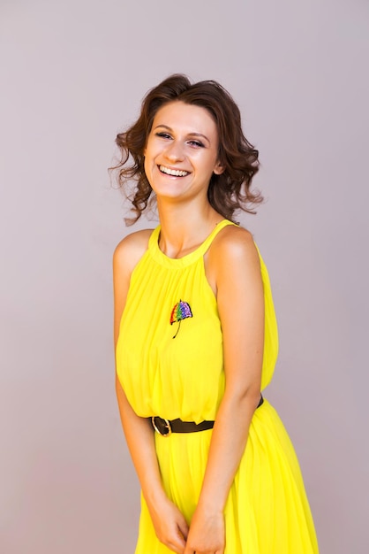 Brooch in the form of a rainbow umbrella on a yellow dress of a brunette girl The girl poses on a gray background laughs and looks into the camera