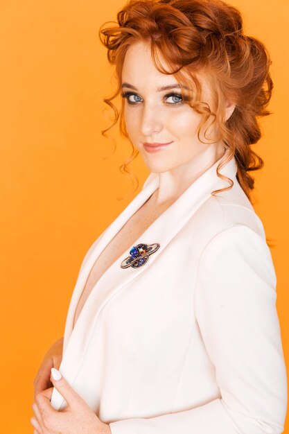 Brooch in the shape of a planet with a ring on the white jacket of a redhaired girl Girl posing on orange background