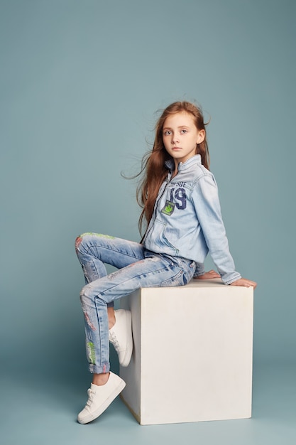 Brooding beautiful girl sitting on a white cube and posing, school models