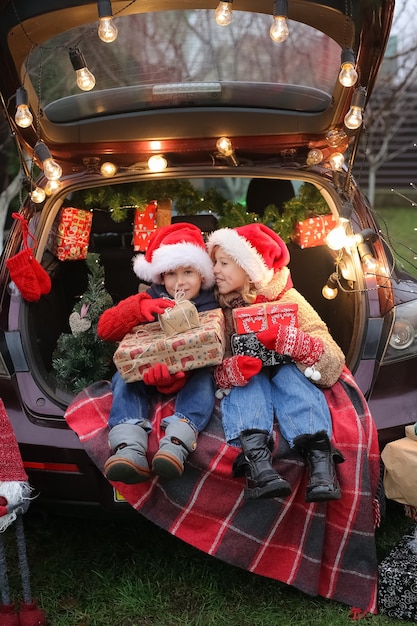 Brother and Sister are sitting in the car decorated with New Years a lot of gift boxes