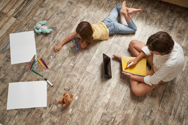 Brother and sister lying on the wooden floor at home and spending time together little girl playing