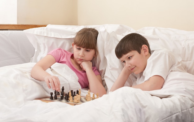 Brother and sister play chess in bed, indoors