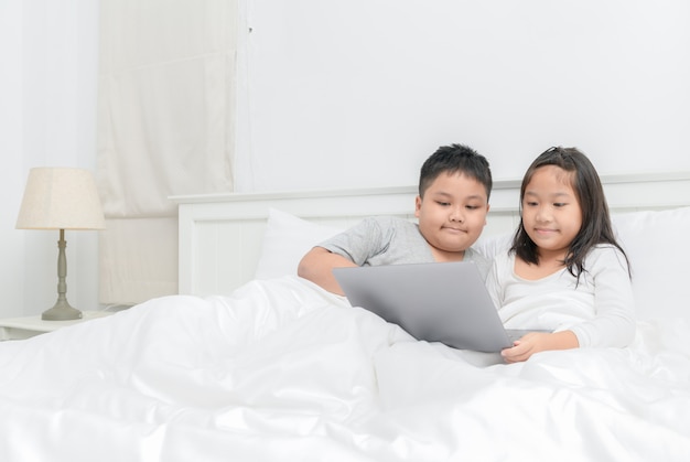 Brother and sister play laptop on bed together