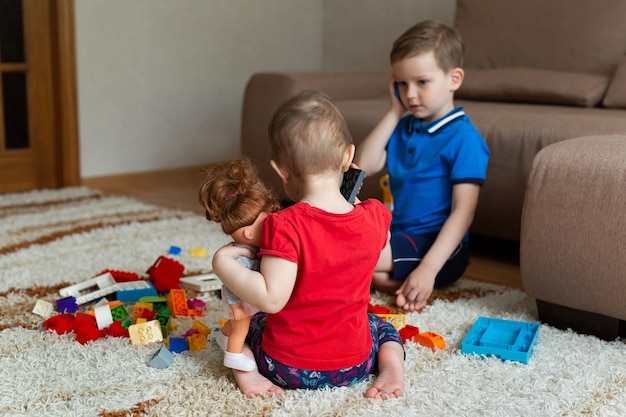 Brother and sister play with a construction kit and talk on a toy phone.