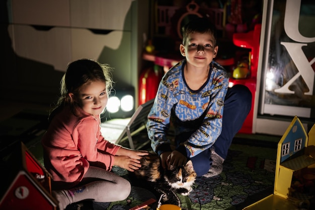 Brother and sister playing with kitty at home during a blackout using alternative lighting