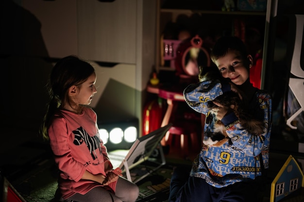 Brother and sister playing with kitty at home during a blackout using alternative lighting