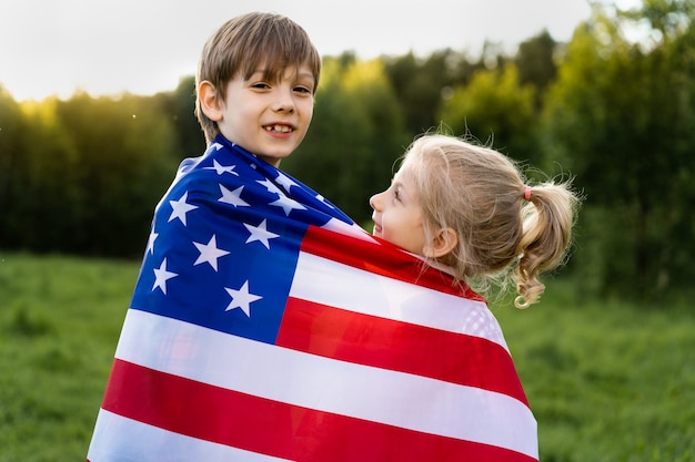 Brother and sister with American flag hug, happy kids on US Independence Day.