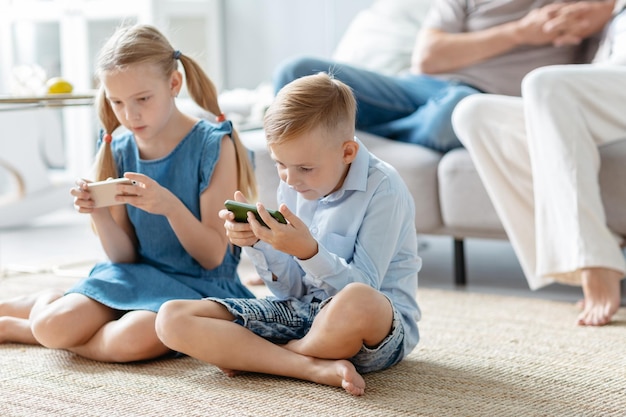 Brother and sister with smartphones sitting on the floor in the living room