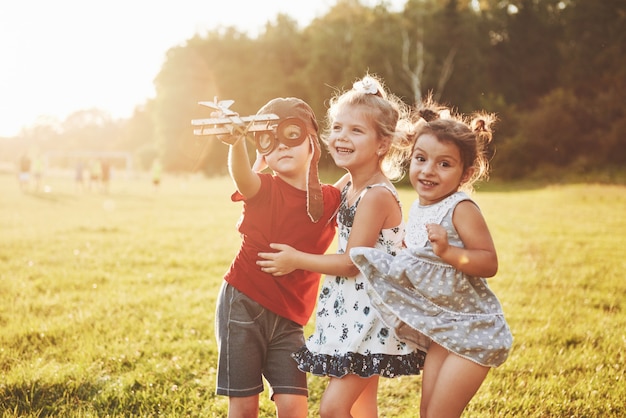 Brother and two sisters are playing together. Three children playing with a wooden airplane outdoor